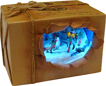Музыкальная композиция "Волшебная посылка", артикул – 52013. Внутри посылки, зимняя деревушка освещена лёгким голубым светом, проигрывается 8 рождественских мелодий, человечки движутся вокруг ёлки. Музыкальная композиция работает от батареек.